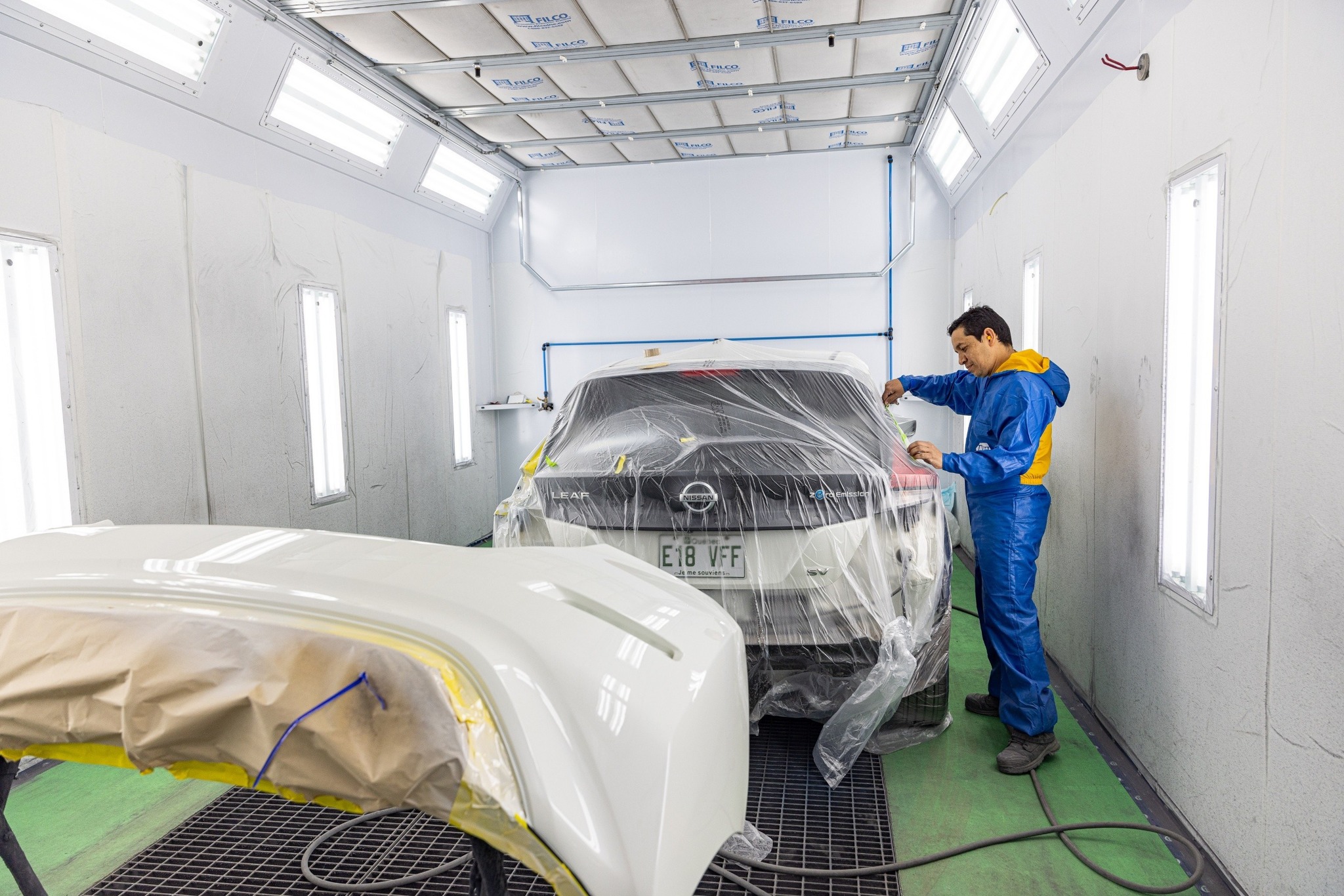 Carrossier ponçant un panneau de carrosserie dans un atelier à Saint-Georges